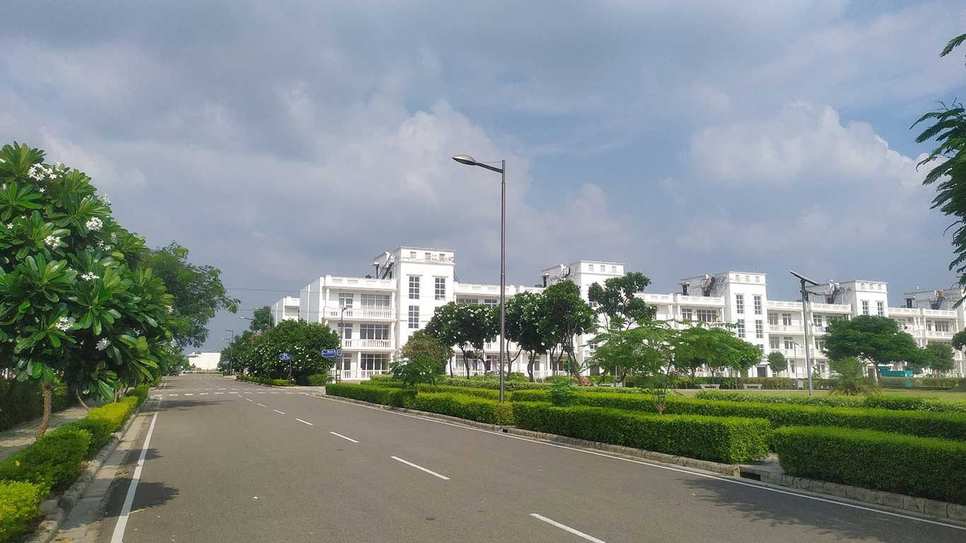 Photograph of white low-rise independent floor buildings beside a landscaped internal road in DLF Hyde Park Estate, New Chandigarh