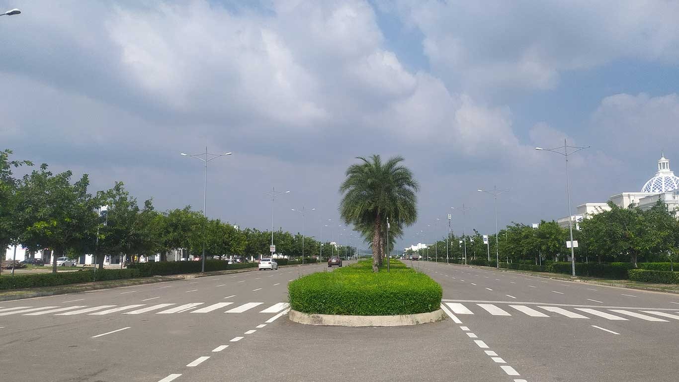 Photograph of a wide divided boulevard with street lights and a palm-planted median inside DLF Hyde Park Estate, with the clubhouse dome at the right