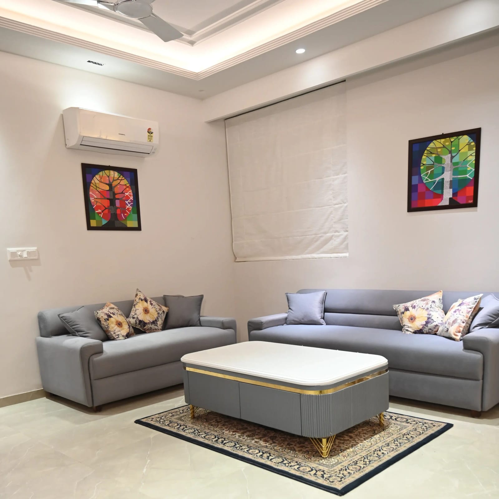 Furnished living room in a Golden Castle flat in Zirakpur with two grey sofas, a centre table and cove-lit ceiling.