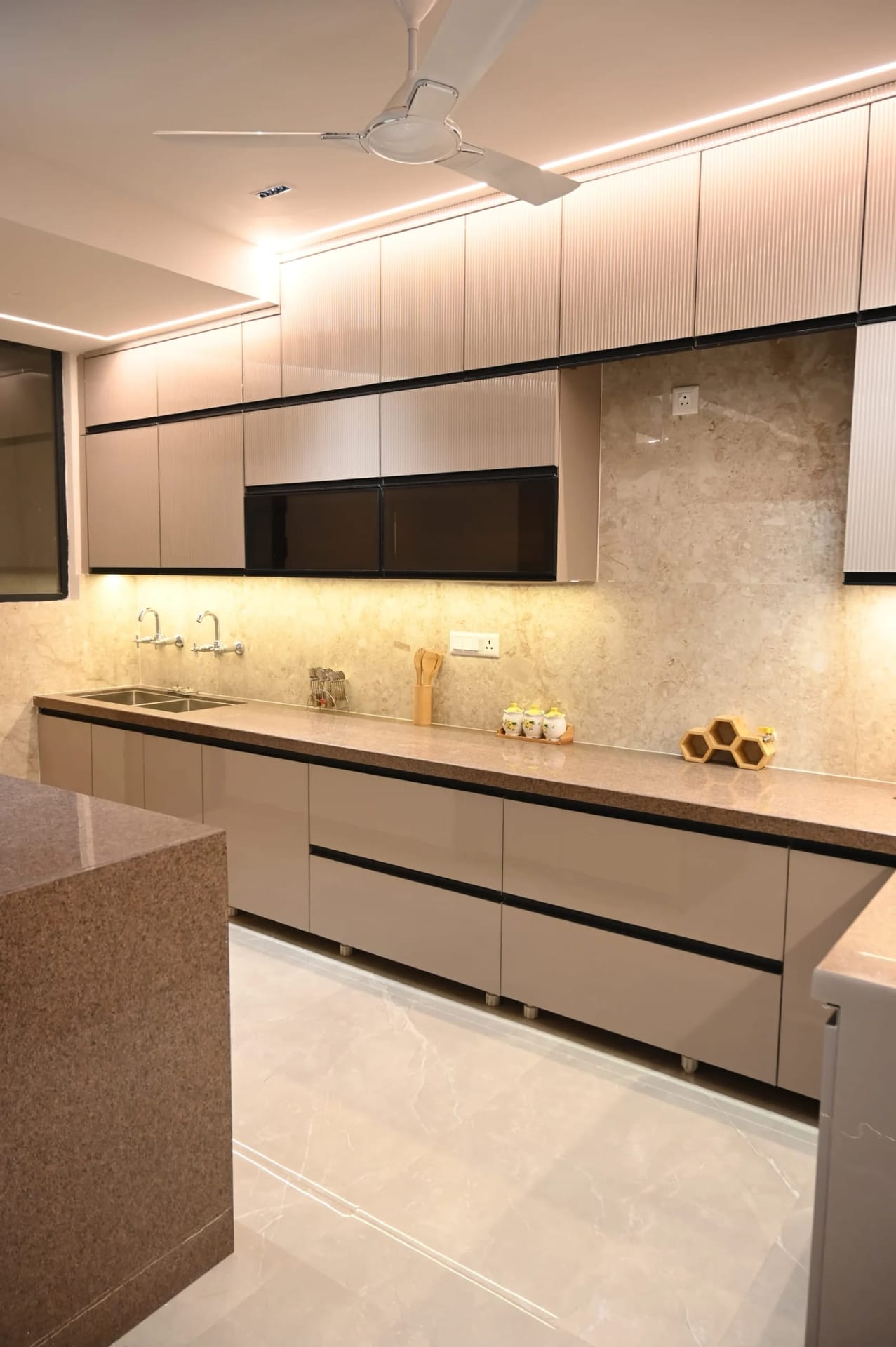 Modular kitchen in a Golden Castle flat in Zirakpur with beige fluted cabinets, stone counter and under-cabinet lighting.
