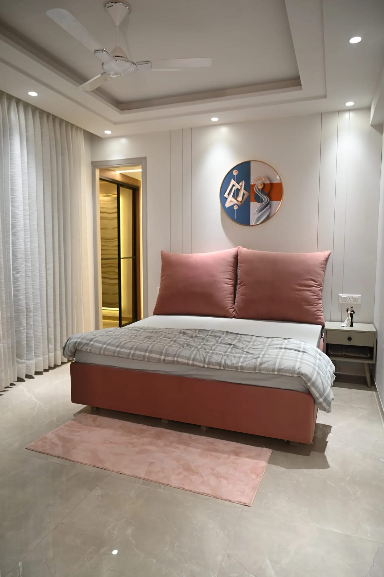 Furnished bedroom in a Golden Castle flat in Zirakpur with a rust-coloured bed, panelled wall and sheer curtains.