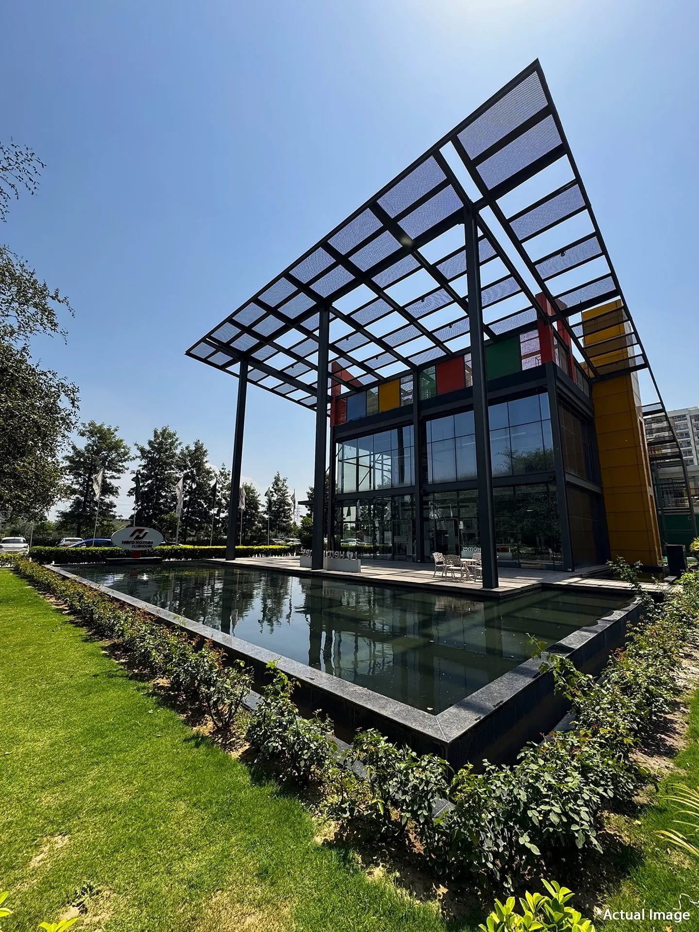 Actual photo of the glass-fronted clubhouse with a canopy roof and reflecting pool at Hero Homes, Sector 88, Mohali