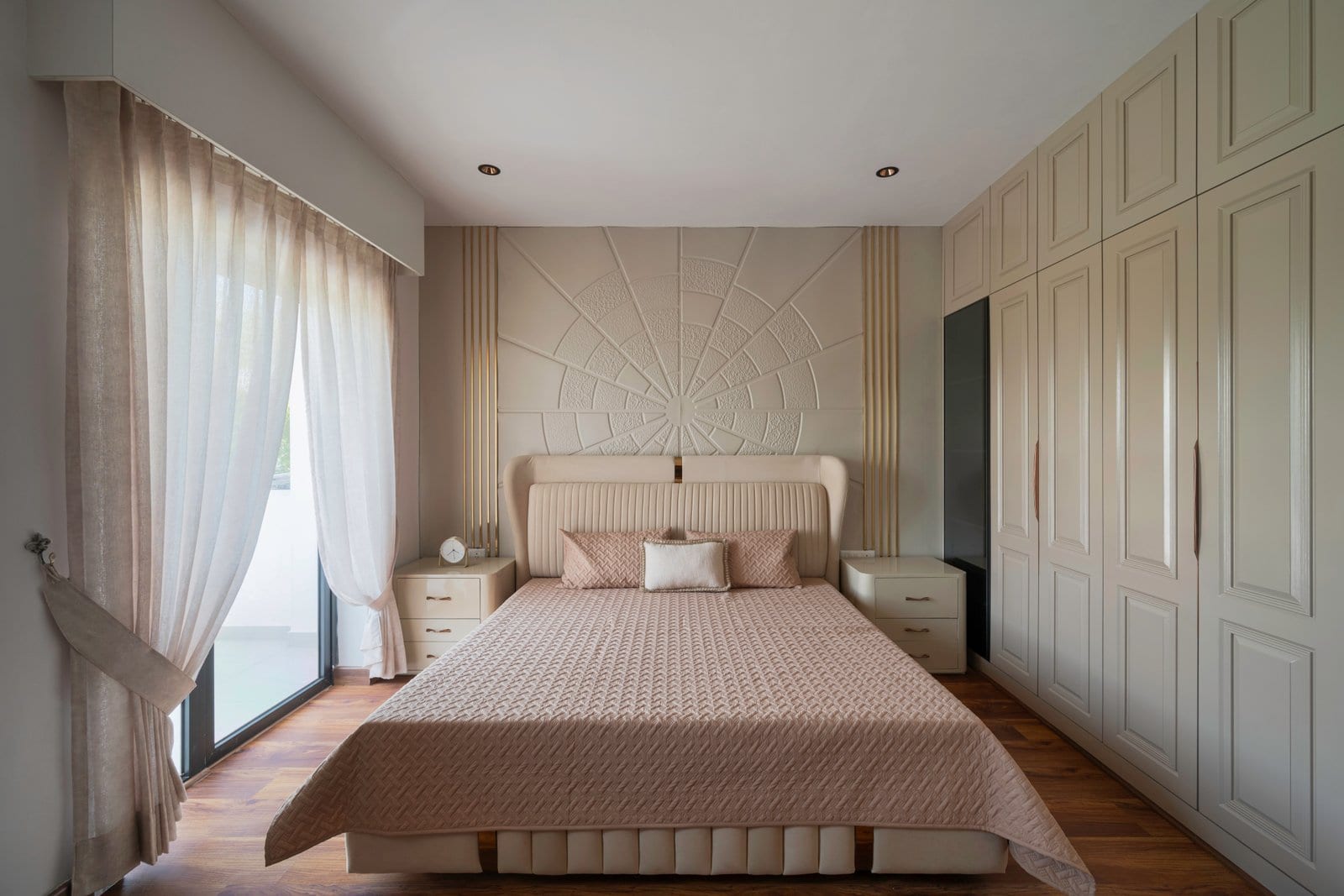 Bedroom of the sample apartment at The Wellness City, Rajpura, with an upholstered bed, carved headboard wall and full-height wardrobes.