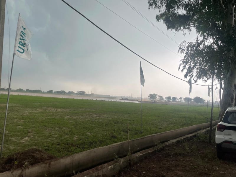 Photo of the open land at the Urvaa Realty site near Rajpura under a cloudy sky, with flags along the edge